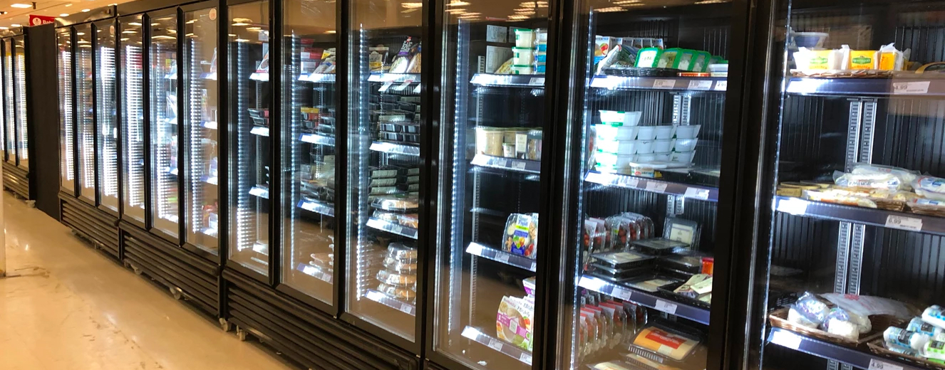 Refrigerated display cases filled with various packaged food items, illuminated with bright white lighting.
