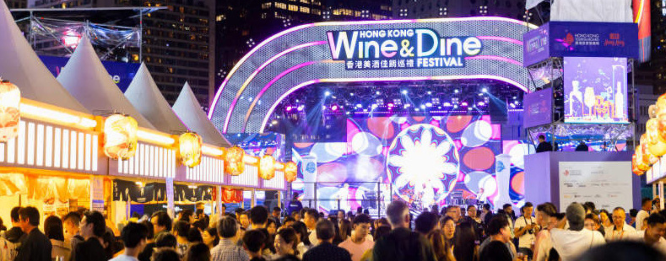 Crowd at the Wine & Dine Festival under vibrant, illuminated signage and colourful lights.