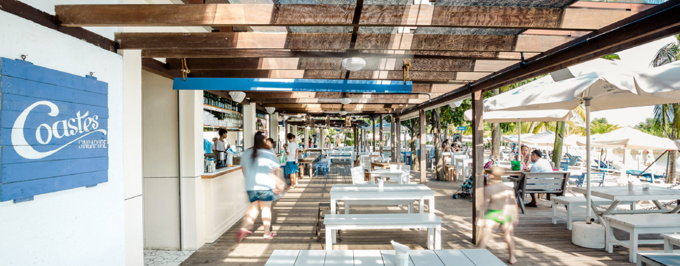 Bright, airy restaurant space with white wooden tables and shaded seating under a pergola.