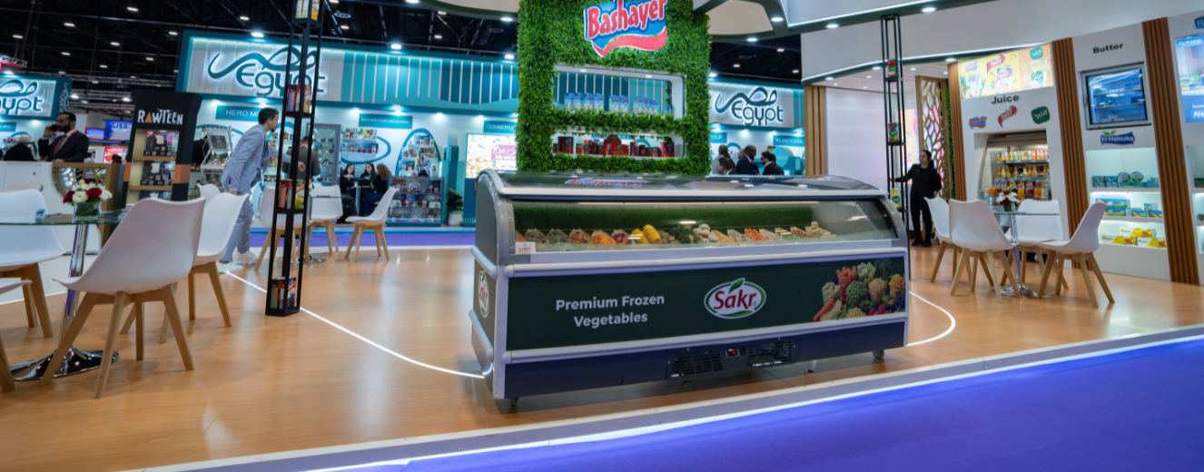 Showcasing a refrigerated display with vibrant vegetables, surrounded by green foliage and branding.