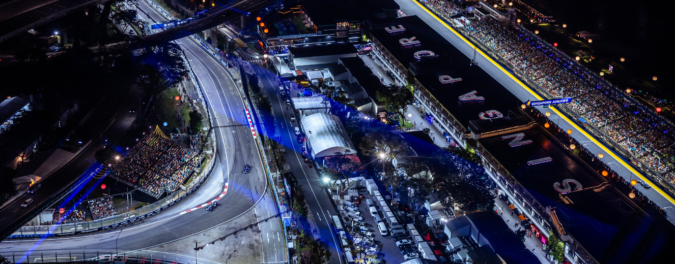 Aerial view of a racetrack illuminated at night, featuring blue lighting and surrounding catering facilities.
