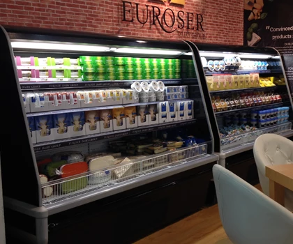 Chilled display cabinet filled with various dairy products and beverages against a brick wall backdrop.