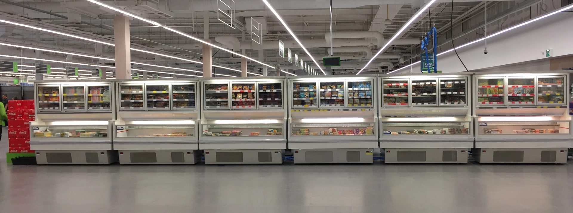 Chilled display units filled with various products, set against a bright, modern supermarket interior.