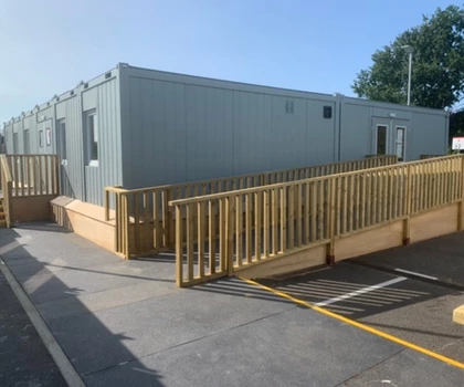 Light green modular building with a wooden ramp, set against a clear blue sky.