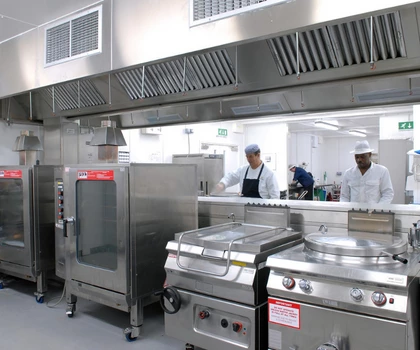 Stainless steel kitchen equipment with chefs in white uniforms working in a large commercial kitchen.