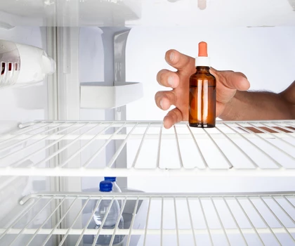 A hand reaches for an amber glass bottle on a white refrigerator shelf.