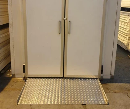 Double white doors with metal handles and a textured silver mat at the entrance.