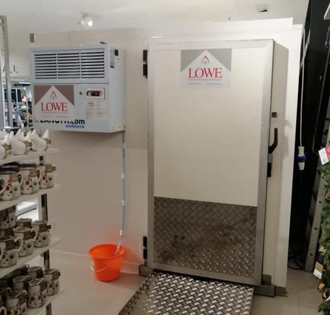 Modular walk-in cold room with a white exterior and metal floor, featuring an orange bucket nearby.