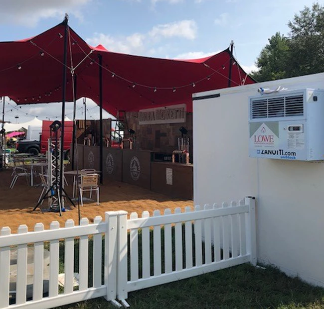 A modular cold room with a white exterior, surrounded by a white picket fence and red canopy.