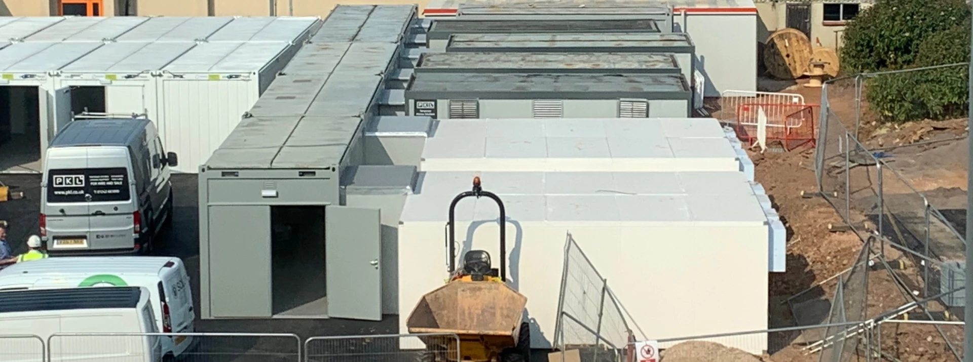 Large commercial kitchen roof with grey metal panels and a yellow construction vehicle in foreground.