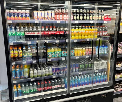 A display fridge filled with various colourful soft drinks and beverages in clear bottles.