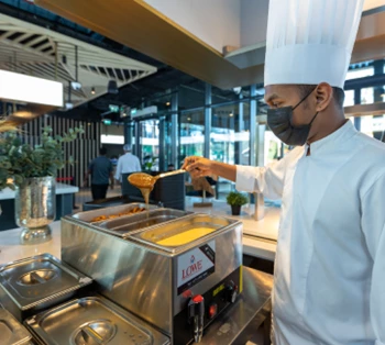 A chef in a white uniform and hat uses a spatula to serve food from a buffet station.