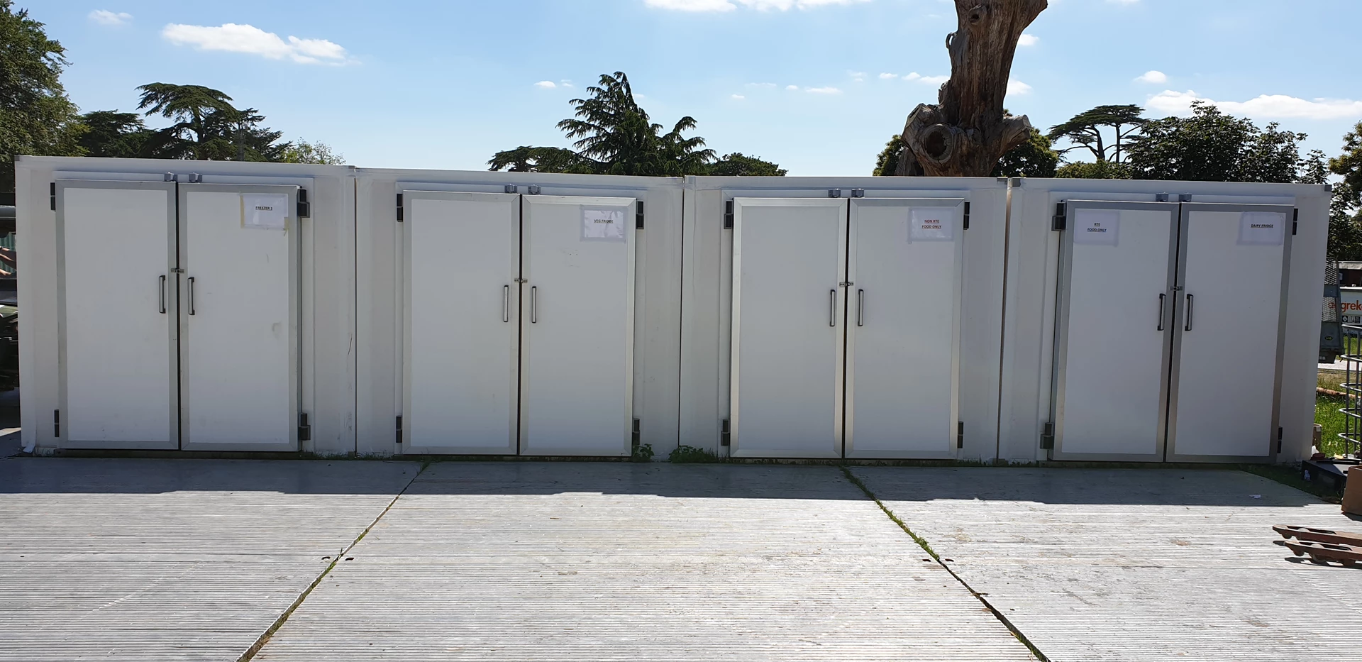 Four white modular walk-in cold rooms are lined up against a clear blue sky.