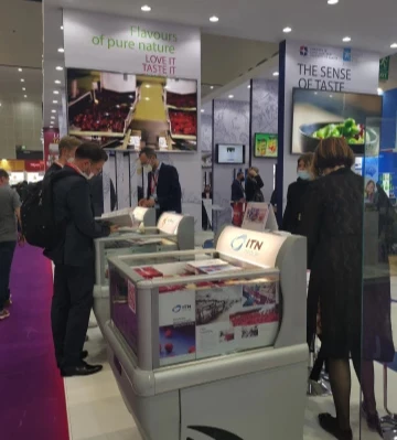 Visitors examine displays at an exhibition, featuring colourful products and bright lighting.