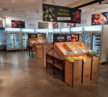 Brightly lit grocery store interior featuring wooden produce displays and frozen food sections.