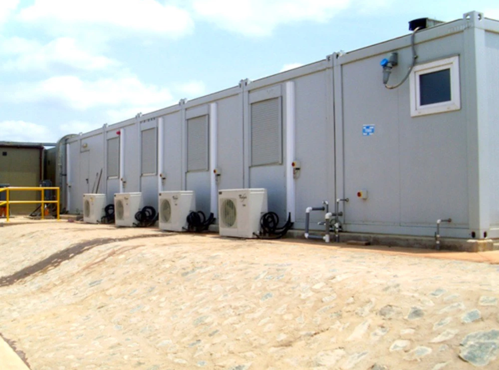 Grey temporary kitchen units lined up, featuring air conditioning units on a sandy surface.