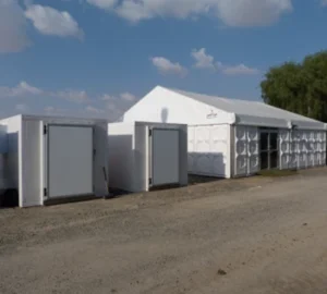 White storage units and a large tent against a blue sky with scattered clouds.