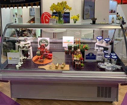 Display case featuring colourful food items, including vegetables and jars, with a bright background.
