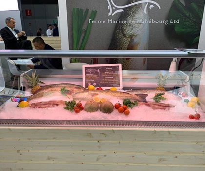 Display of fresh fish on ice, surrounded by colourful garnishes and a promotional sign in the background.