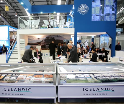 Exhibition booth featuring a blue backdrop, with people engaging around displays of Icelandic products.