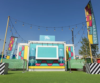 Vibrant outdoor event stage with colourful decorations, green grass, and blue sky above.
