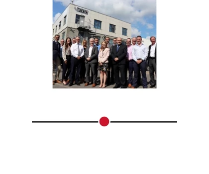 Group of professionals in formal attire standing outside a modern building under a blue sky.