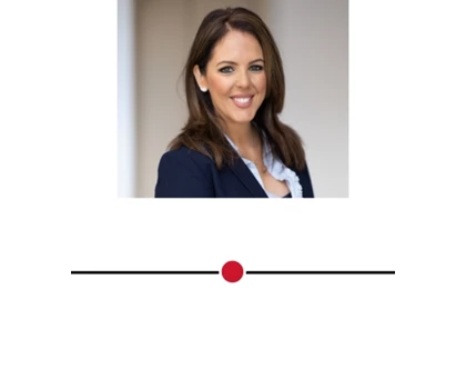 Smiling woman with brown hair, wearing a navy blazer and white blouse, against a neutral background.
