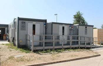 Three grey temporary kitchen units with white doors, set on a grassy area under clear blue skies.
