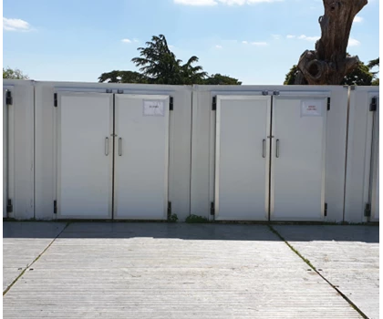 Three white storage units against a clear blue sky, with green grass visible in the background.