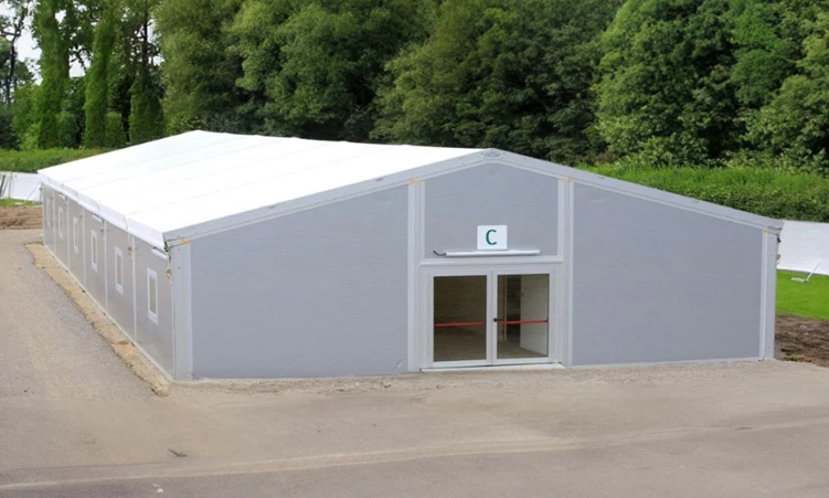 Temporary grey kitchen structure with a white roof, set against a backdrop of green trees.