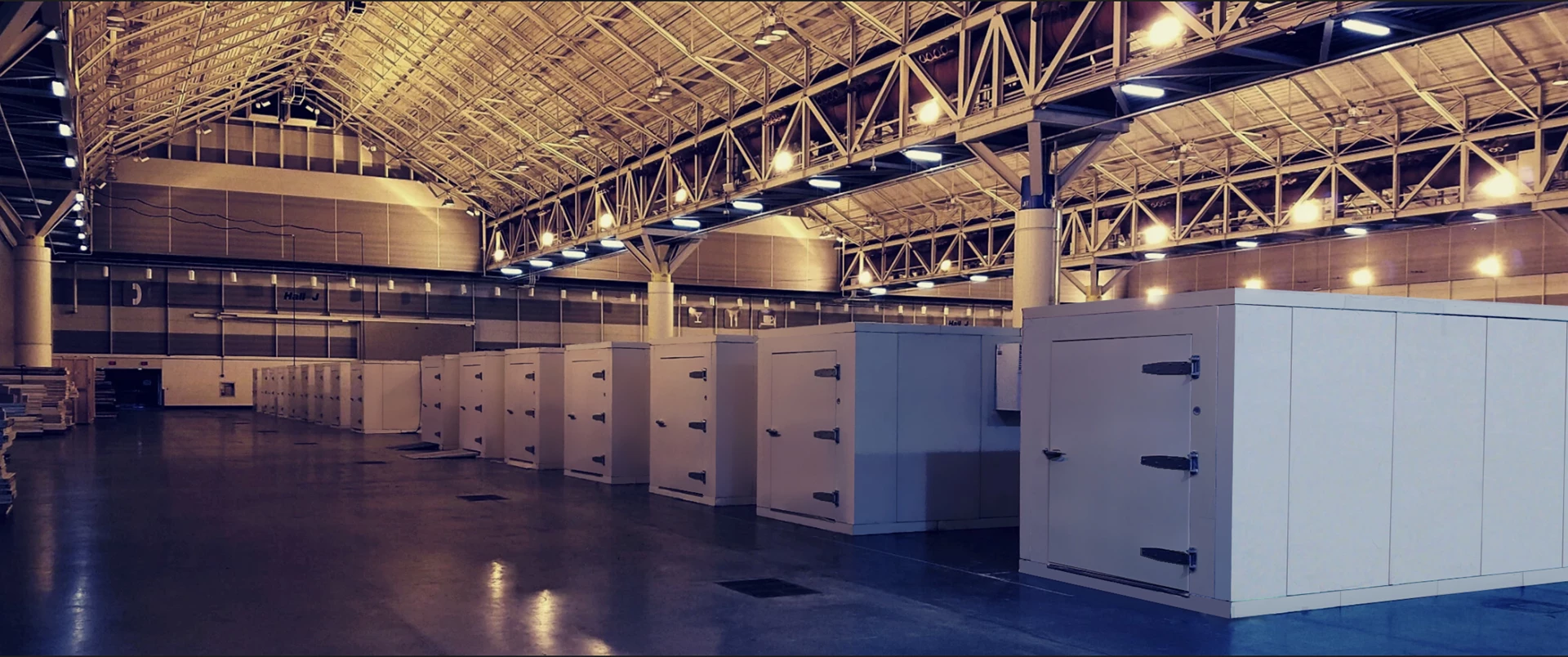 White cold storage units lined up in a spacious industrial facility with a high ceiling.