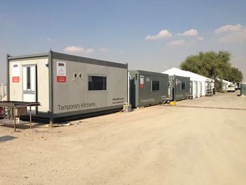 Temporary grey structures line a dirt path under a clear blue sky at the Dubai Rugby 7s.