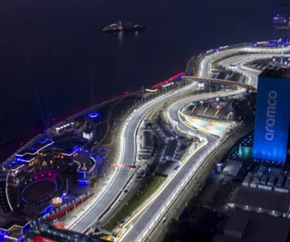 Aerial view of a brightly lit winding road at night, with water and buildings in the background.