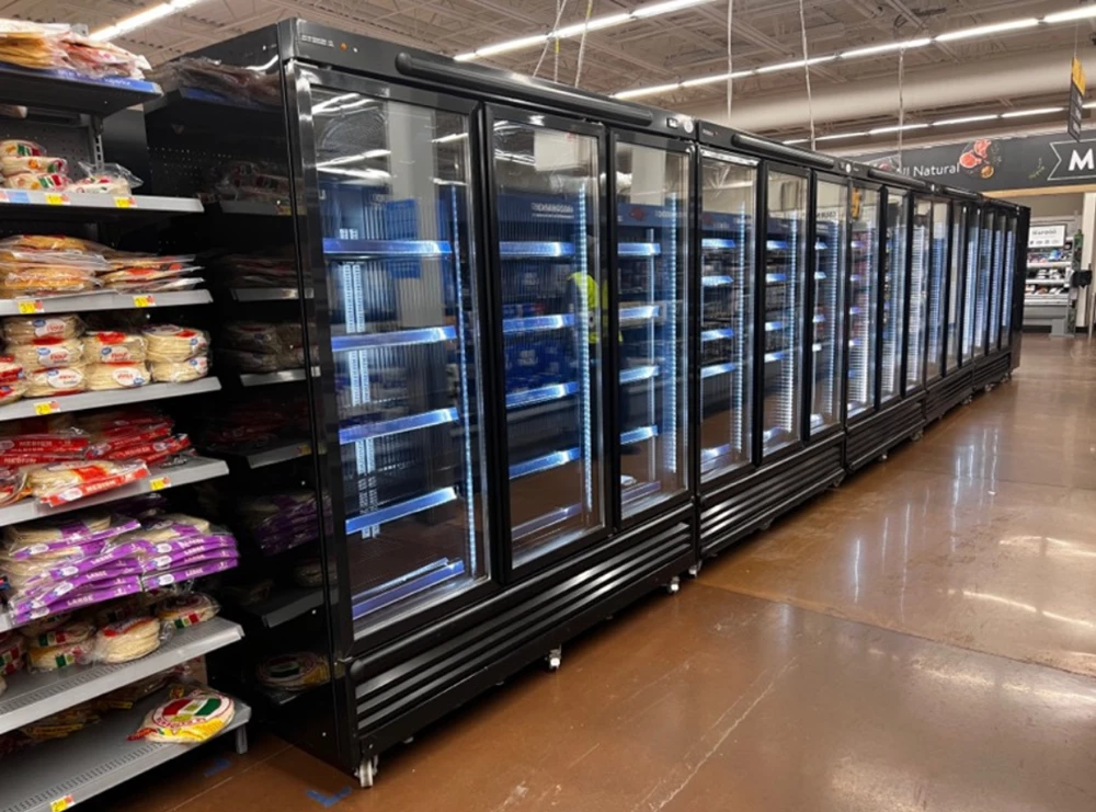 Black glass-fronted refrigeration units line a retail space, showcasing various packaged products.