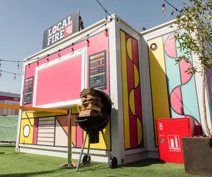 Colourful food stall with a pink backdrop, featuring a grill and vibrant geometric designs.