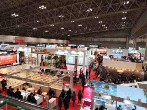 Aerial view of a busy exhibition hall with red carpet, featuring various vendor booths and attendees.