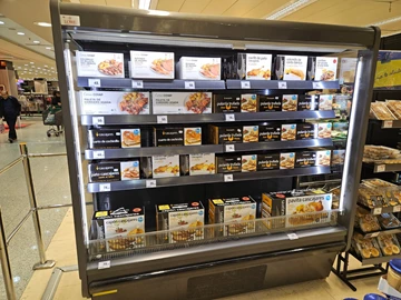 A refrigerated display case filled with various packaged meals, featuring black and white product designs.