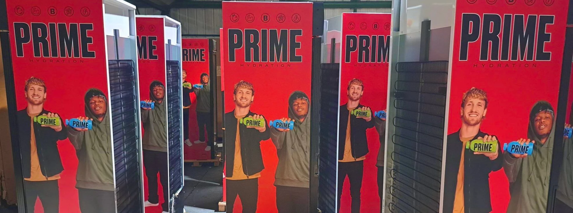 Two men holding drinks stand in front of vibrant red promotional banners for Prime Refrigeration.