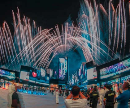 Spectacular fireworks illuminate a night sky, with vibrant blue and pink bursts over a bustling crowd.
