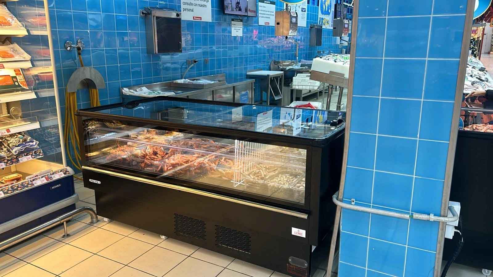 Black refrigerated display case filled with various food items, set against blue tiled walls.
