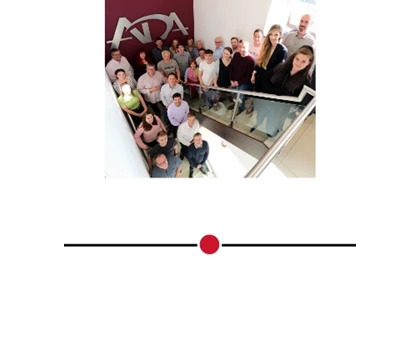 Group of people gathered on a staircase, with a maroon wall featuring a logo in the background.