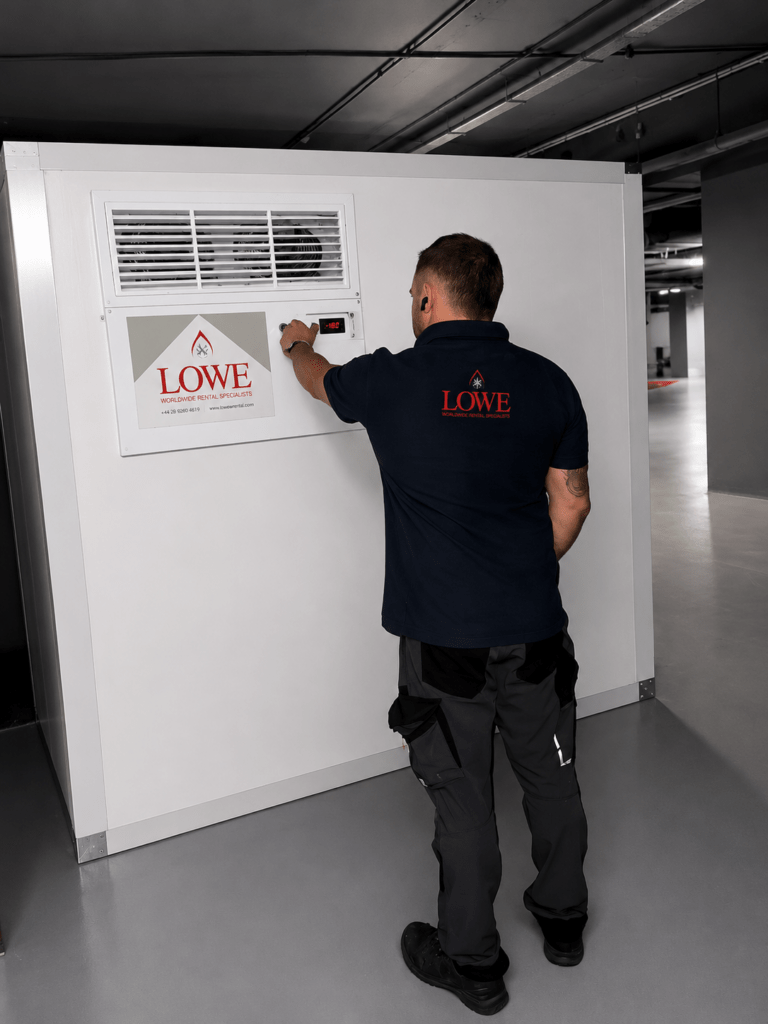 A man in a navy shirt adjusts a panel on a white wall, labelled "LOWE.