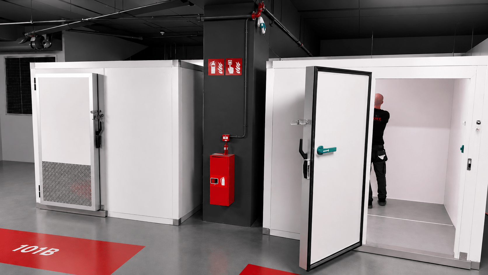 White storage units with a red fire extinguisher and green door handle in a grey setting.