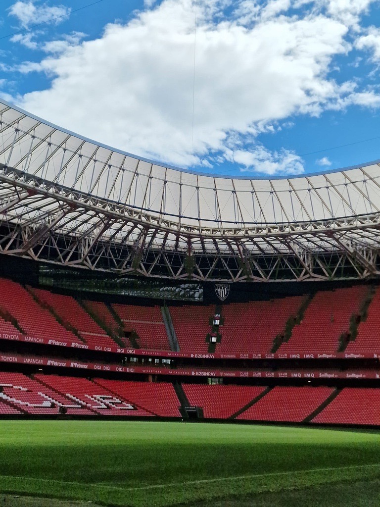 Interior of a stadium featuring a red seating area and a bright blue sky above.