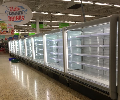 Empty refrigerated display cases with bright white lighting in a supermarket aisle.