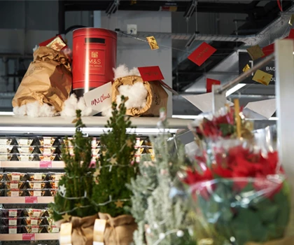 Festive display featuring small Christmas trees and red decorations in a supermarket setting.