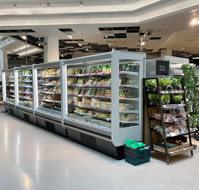 Chilled display units filled with packaged food items, alongside a shelf of fresh produce.