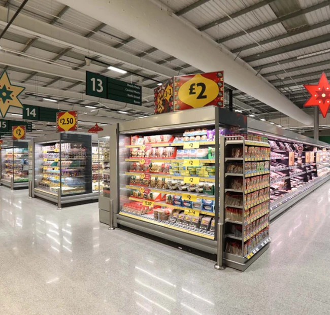 Brightly lit supermarket aisle featuring refrigerated displays and shelves stocked with various products.