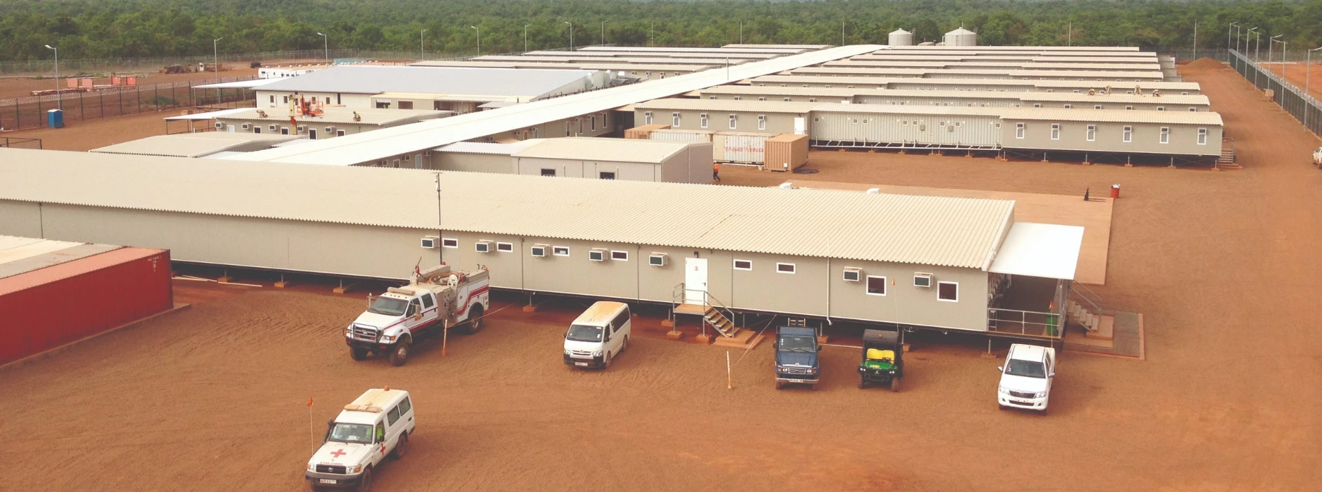 Single-storey buildings with light-coloured exteriors on reddish-brown soil, surrounded by greenery.