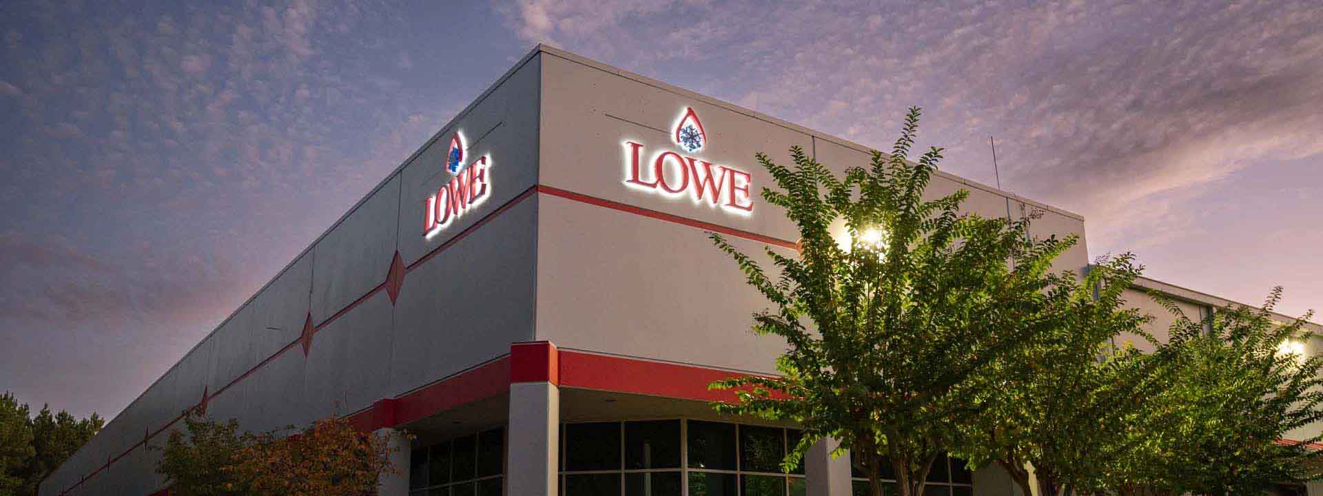 Lowe's store exterior with illuminated signage, surrounded by greenery under a twilight sky.